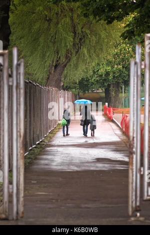 La madre sta prendendo i suoi figli a scuola in un giorno di pioggia a Tallinn in Estonia. hanno appena attraversato il cancello in acciaio del campo sportivo. Foto Stock