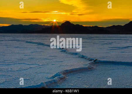 In questa foto un'pressione" colmo di sale i serpenti fuori attraverso la Bonneville Saline come il sole tramonta sulla isola di argento montagne in distanza. Foto Stock