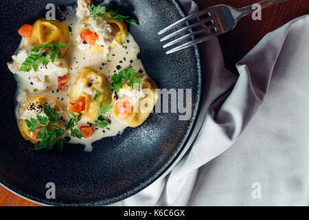 Vista ravvicinata di bollito in casa gnocco di carne servita nella piastra di argilla gnocchi di patate con salsa cremosa e cucchiaio di legno. composizione in stile rustico in legno Foto Stock