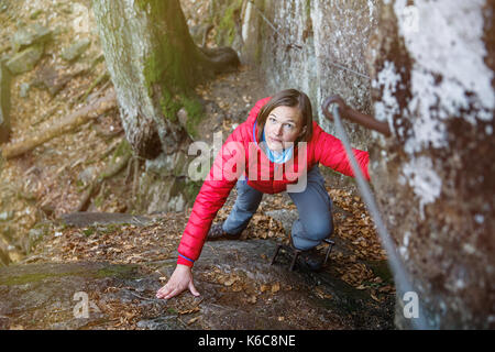 Donna rock climbing nella foresta, tenendo la ringhiera di protezione, la risalita verso l'alto, riuscendo. Uno stile di vita attivo, il progresso e il miglioramento, conquista Foto Stock