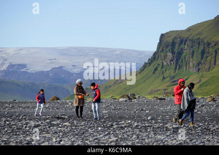 I turisti alla spiaggia di Reynisfjara, una delle attrazioni turistiche più famose in Islanda, e il cappuccio di ghiaccio che copre il vulcano Katla. Foto Stock