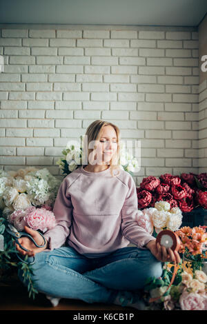 Carino bella giovane donna fioraio seduti nella posizione del loto in negozio di fiori. Foto Stock