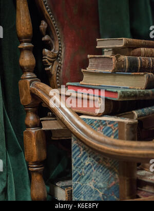 Vintage poltrona in stile barocco con vecchi libri contro la cortina verde Foto Stock