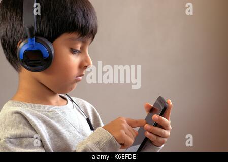 Bambino utilizzando smart phone. Kid che indossano le cuffie guardando sullo smartphone. Kid toccando il touchscreen. Foto Stock