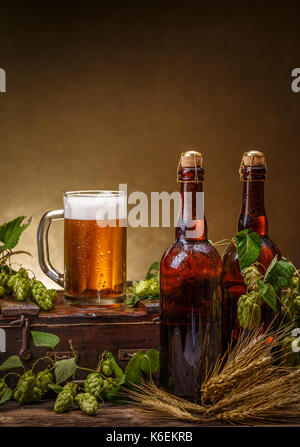Il vetro e le bottiglie di birra con il luppolo sul tavolo di legno Foto Stock