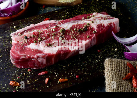 Primo piano di una striscia di greggio steak conditi con spezie differenti, quali ad pepper calli di differenti colori oppure origano, su un rustico in legno scuro vassoio Foto Stock