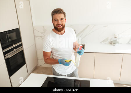 Felice l'uomo barbuto vicino alla stufa con i detergenti che guardando la telecamera Foto Stock
