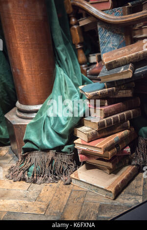 Pila di libri vecchi con sedia in legno e cortina verde Foto Stock