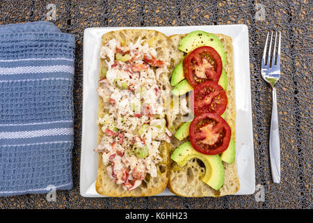 Un tempo estivo trattare di un rotolo di astice. fatta con carne di astice, un po' di mayo, tagliata a fette di avocado e pomodoro a fette. servita su una ciabatta rotolo su un bianco Foto Stock