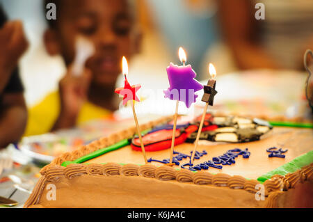 Torta di compleanno con tre candele accese e fuori fuoco persone Foto Stock