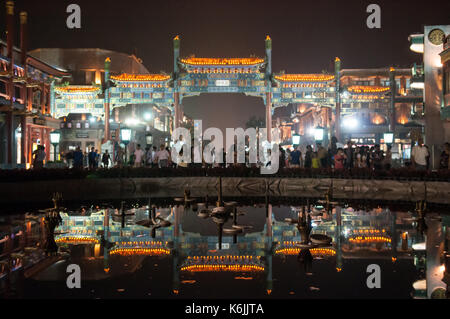 La folla di pedoni a piedi attraverso il cinese tradizionale gateway paifang all'entrata di qianmen street, riflesso nelle acque di una fontana a Foto Stock