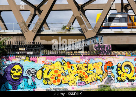 Scena urbana del treno (motion sfocata) attraversando ponte trave passante parete ricoperta in graffiti nella zona est di Londra Foto Stock