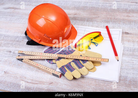 Orange elmetto, occhiali di sicurezza e guanti protettivi e nastro di misurazione su sfondo di legno. Foto Stock