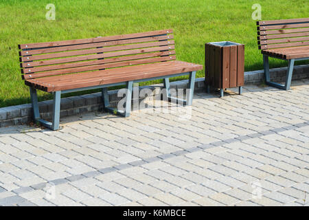 Due eleganti panchine e un cestino in estate il parco lungo un percorso lastricato contro un prato verde. piccole forme architettoniche concept Foto Stock