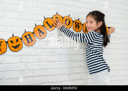 Dolce bambini aiutare la sua famiglia a riagganciare la decorazione a celebrare la festività di halloween a casa. Foto Stock