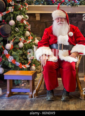 Sant in attesa per i ragazzi per ottenere la loro vacanza shot su cui si fa clic in una piscina impostazione. lo sfondo mostra un albero di Natale decorato con ornamenti su di esso. Foto Stock