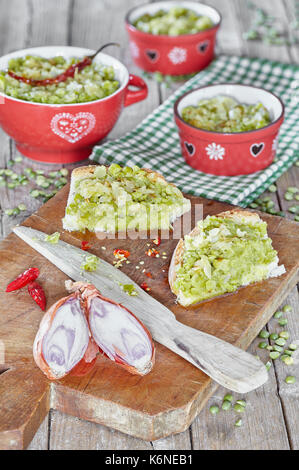 Crema Verde di piselli spezzati con salsa di olio di oliva e cipolle fritte, in piccole ciotole e spalmato su fette di pane. Foto Stock