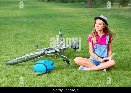 Colpo di una giovane e bella donna ciclista in appoggio sull'erba al parco dopo il ciclo di lettura di un libro sorridente felicemente la ricreazione hobby letteratura int Foto Stock