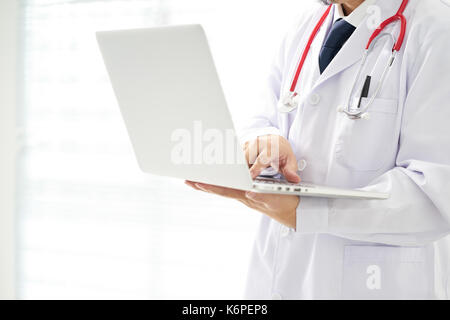 Medico sconosciuto in posa utilizzando laptop con sfondo luminoso, indossa uno stetoscopio . Foto Stock