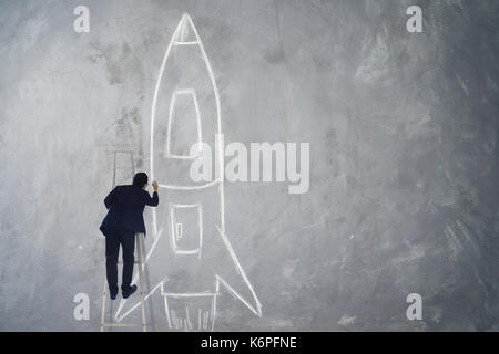 Imprenditore salire scale razzo di disegno disegna sulla parete , il successo, leader e vincitore concetto . Foto Stock