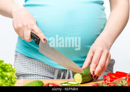 Giovane donna incinta con un coltello in mano si prepara un utile insalata, mani close-up Foto Stock