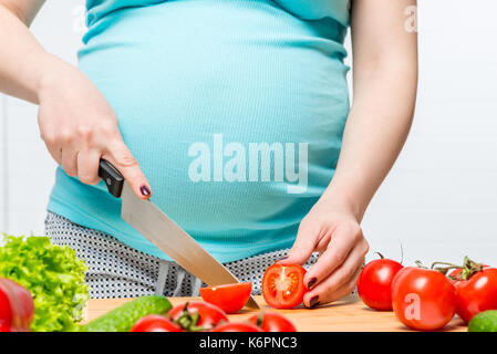 Ragazza con una grande pancia prepara una insalata di verdure su un tavolo Foto Stock