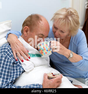 L'anziano bedridden uomo è dato un drink dal suo caregiver e moglie Foto Stock