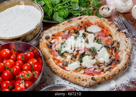 Pizza capricciosa con carciofi, prosciutto e funghi su uno sfondo di legno Foto Stock