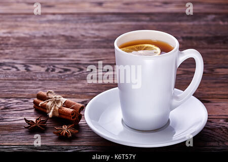 Porcellana Bianca tazza di tè con bastoncini di cannella, limone, foglie di menta e filtro di tè di legno sul tavolo rustico. Foto Stock
