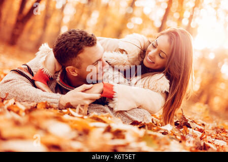 Bella coppia sorridente godendo nella soleggiata foresta in autunno colori. Essi sono giacenti su cascate di foglie e di divertimento. Foto Stock