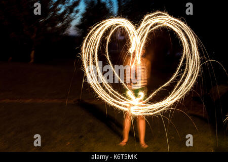 Ragazza facendo un cuore irregolare di scintille con luci di bengala. sfondo sfocato Foto Stock