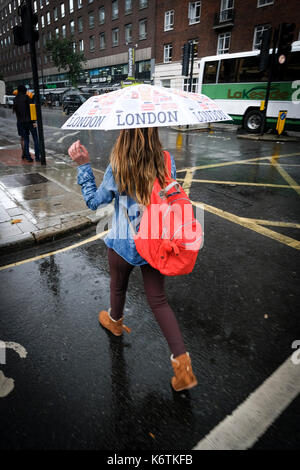 Ragazza di strada di attraversamento in heavy rain holding ombrello di Londra Foto Stock