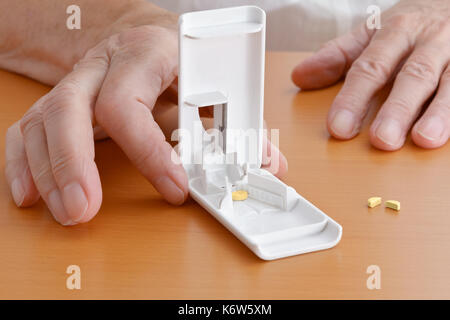 Due mani su un tavolo in legno tenendo un plastico bianco pillola o compressa fresa, una pillola all'interno, uno diviso a metà accanto a Foto Stock