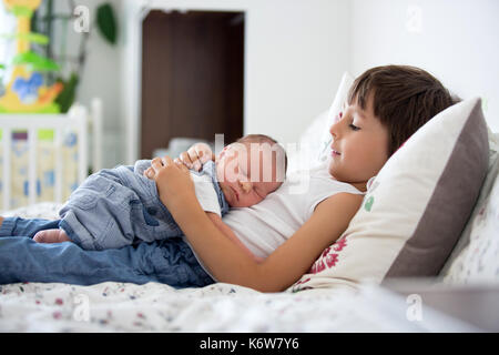 Bel ragazzo, abbracciando con tenerezza e cura il suo neonato fratello a casa. famiglia felicità amore concetto Foto Stock