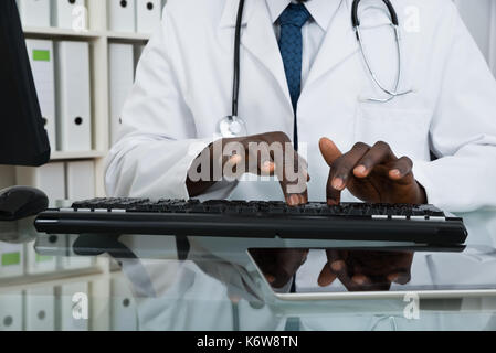 Close-up del maschio africano medico digitando sulla tastiera del computer alla reception Foto Stock