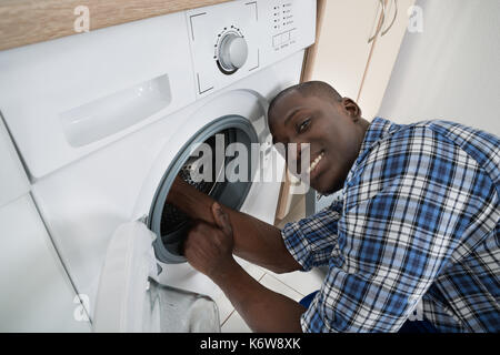 Close-up del giovane africano il tecnico di riparazione della macchina di lavaggio Foto Stock