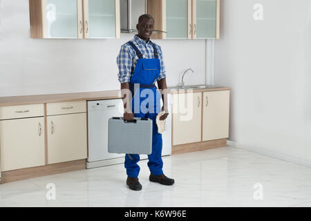Giovani felici tecnico africano holding toolbox in camera con cucina Foto Stock
