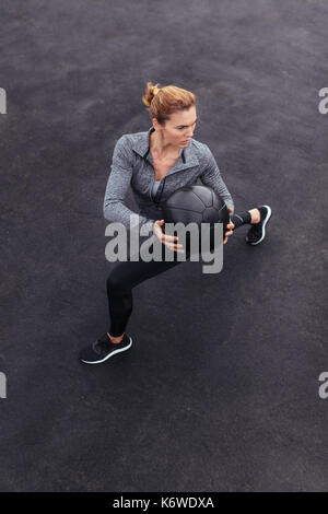 Montare e forte di lavoro femminile fuori con la palla medica. Donna facendo crossfit allenamento all'aperto. Foto Stock