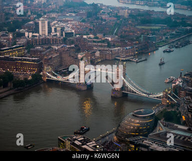 Vista di aperto e illuminato il Tower bridge attraverso il fiume Tamigi, con London city hall, sera, Londra, Inghilterra Foto Stock