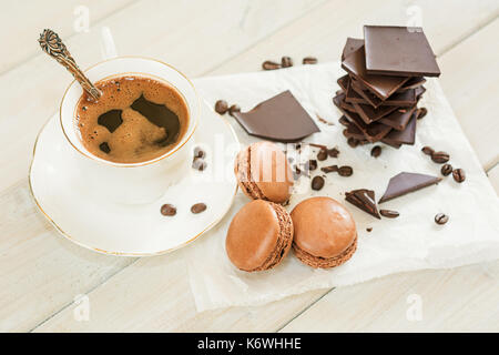 Pezzi di cioccolato con una tazza di caffè presentata su un tovagliolo bianco decorato con sciolto i chicchi di caffè e caffè aromatizzati macarons Foto Stock