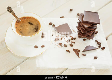 Pezzi di cioccolato con una tazza di caffè presentata su un tovagliolo bianco decorato con sciolto i chicchi di caffè Foto Stock