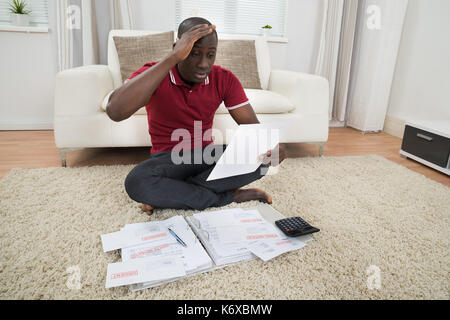 Ritratto di giovane preoccupato african uomo seduto su un tappeto guardando il documento Foto Stock