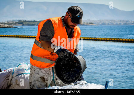 Salumi, Atene, Grecia - Settembre 13, 2017: i lavoratori provare a pulire l'olio che è lavato a terra, su una spiaggia di isola di Salamina vicino ad Atene, dopo un vecchio ta Foto Stock