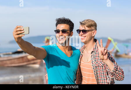 Turisti uomo giovane tenendo selfie foto nella parte anteriore della barca dalla coda lunga sulla spiaggia sul cellulare smart phone, due giovani ragazzi sorridenti sul mare vacanza Foto Stock