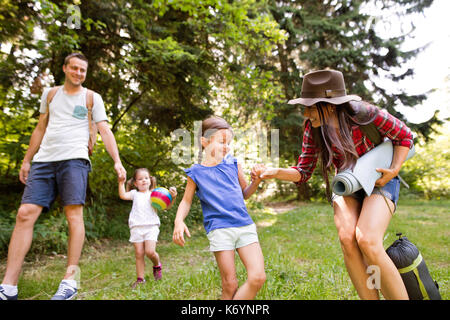 Giovane e bella famiglia con graziosi piccole figlie andare in campeggio foresta. Foto Stock