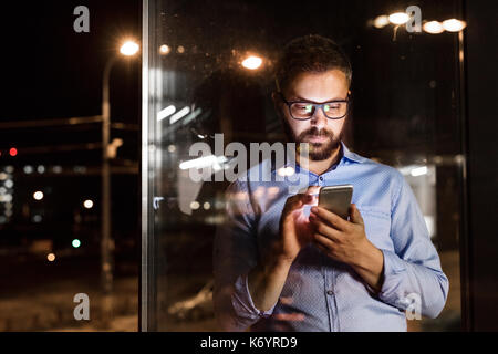 Riflessivo hipster imprenditore con smart phone nel suo ufficio a lavorare fino a tarda notte. Foto Stock