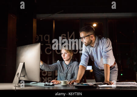 Due giovani imprenditori in ufficio al lavoro notturno in ritardo, a discutere di un progetto. Foto Stock