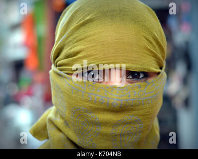 Giovane donna indiana con gli occhi belli copre i capelli e il viso con un velo alla moda secolare, giallo e posa per la macchina fotografica. Foto Stock