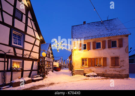 Un vicolo con semi-case con travi di legno e le luci di Natale di notte durante la nevicata a Lachen, neustadt an der Weinstrasse, Germania. Foto Stock