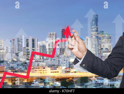 Mano di proprietari utilizzando una penna blu rivolta alla freccia superiore grafico su sfondo di edifici alti in Twilight time,concetto di investimenti e profitti. Foto Stock